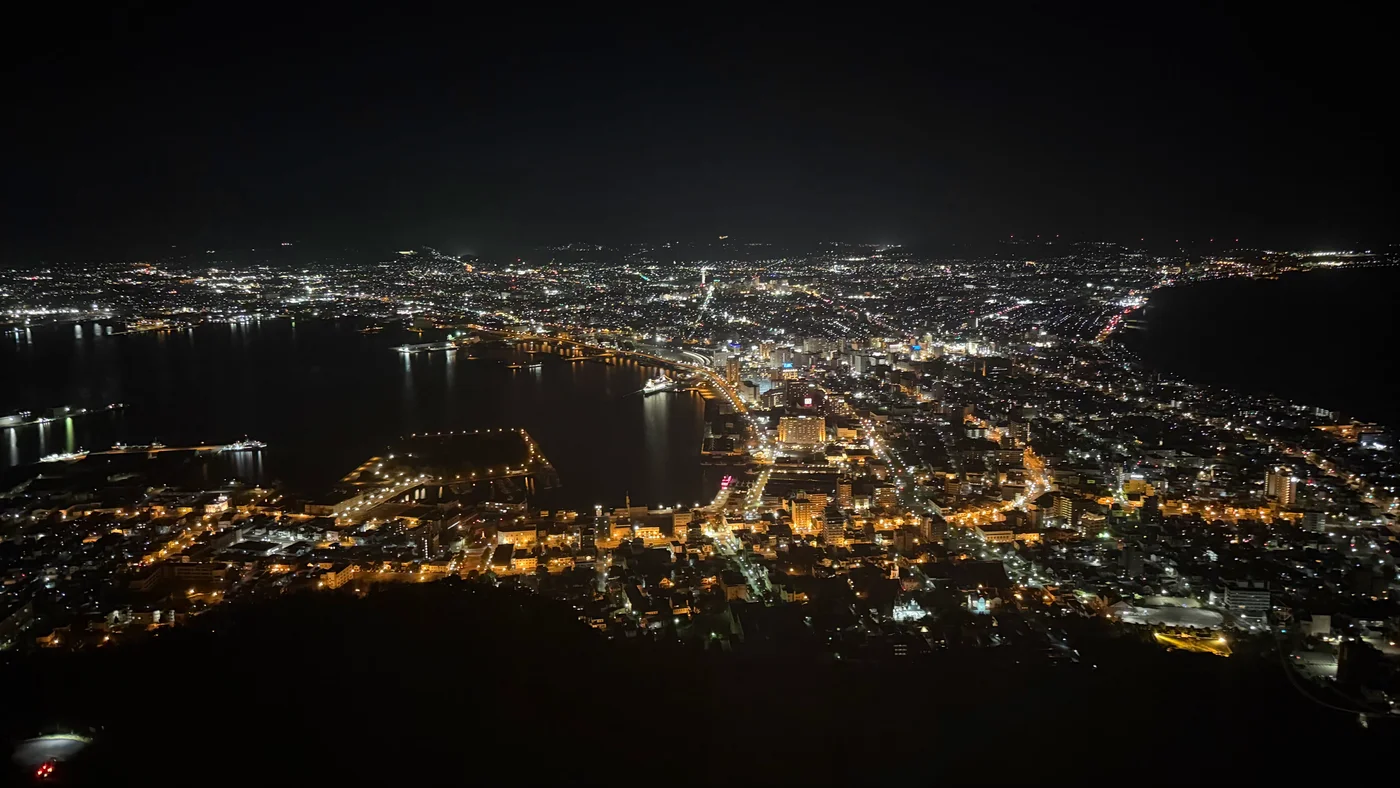 Night view from the summit of Mt. Hakodate, city lights tracing the narrow isthmus between Hakodate Bay and the open sea.